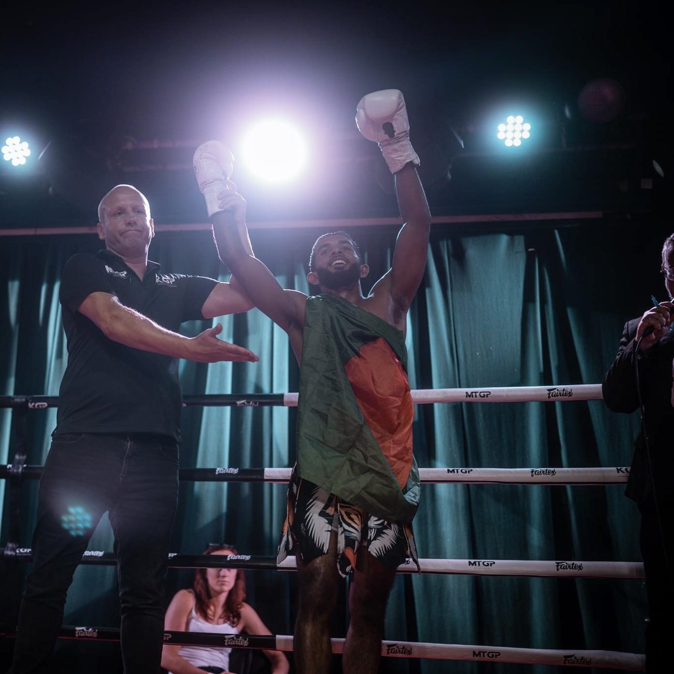 Hasib Bin Tareq in the ring after a win, the Bangladesh flag over his shoulders and his hand raised by the referee.